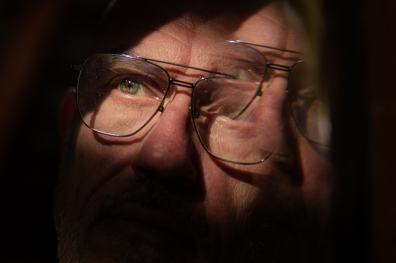 Porträt eines Mannes mit Brille im Licht und Spiegelung, nachdenklicher Ausdruck, Nahaufnahme.
