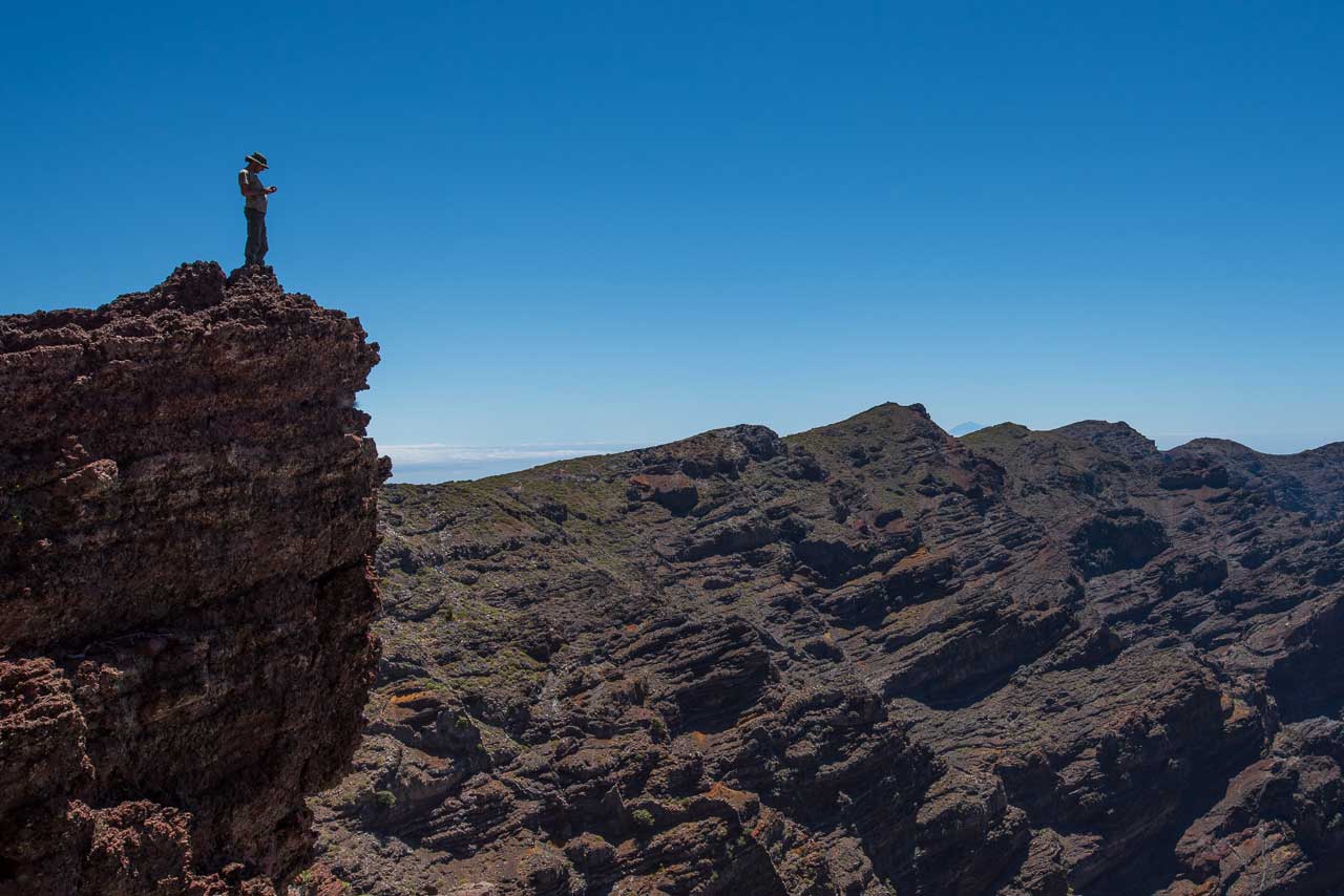 Person steht allein auf einer Felskante vor weiter Gebirgslandschaft unter klarem Himmel – Symbol für innere Stille und Weite.