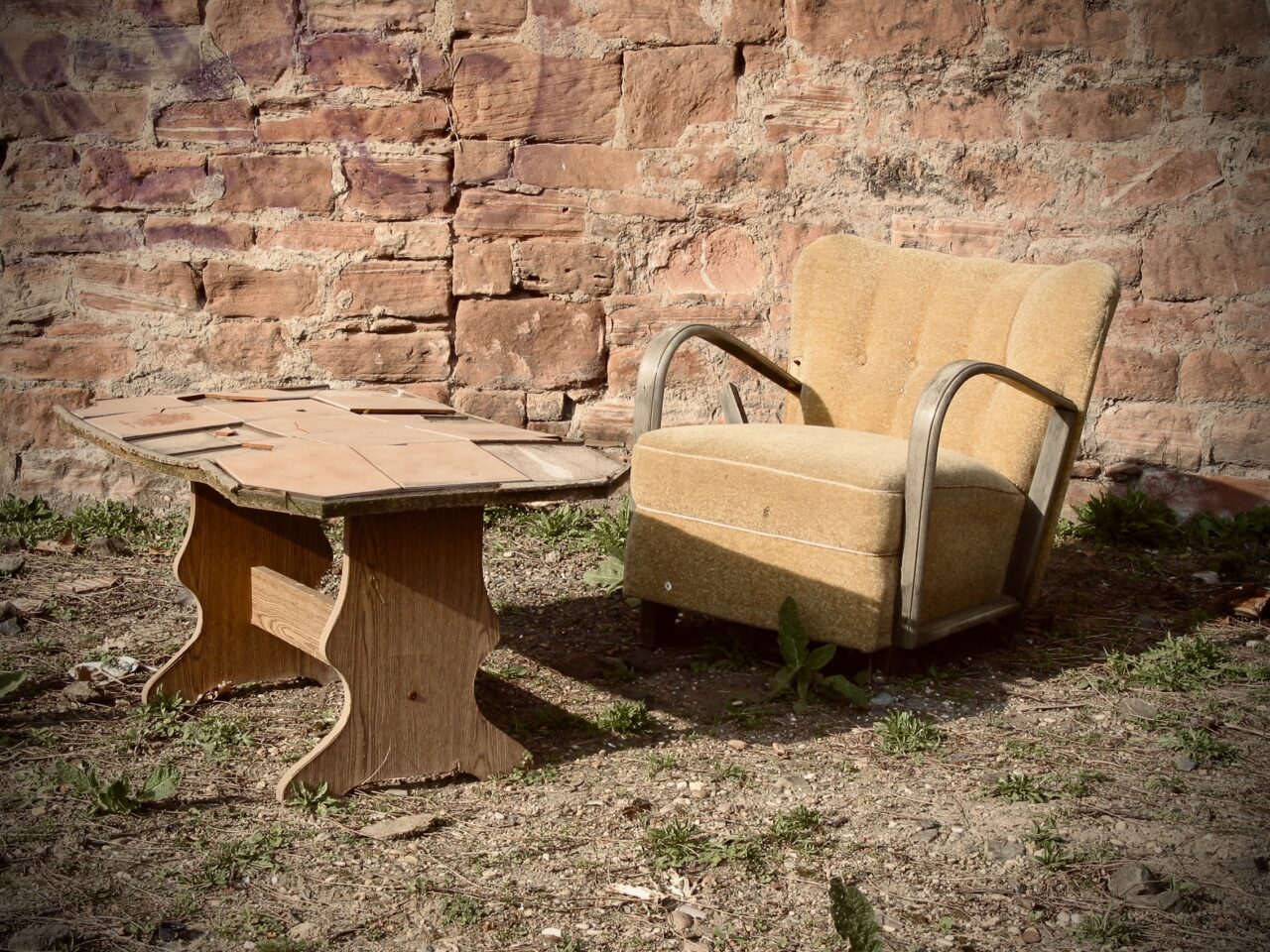 Verlassene Stühle und Tisch in der Natur vor einer alten Mauer.