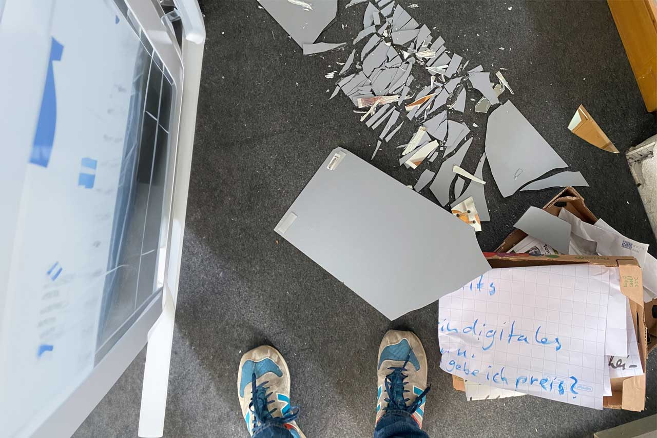 Zerbrochene Glasscheibe, Papier mit handgeschriebenem Text und Sneaker auf grauem Boden – Sinnbild für Brüche im digitalen Raum.