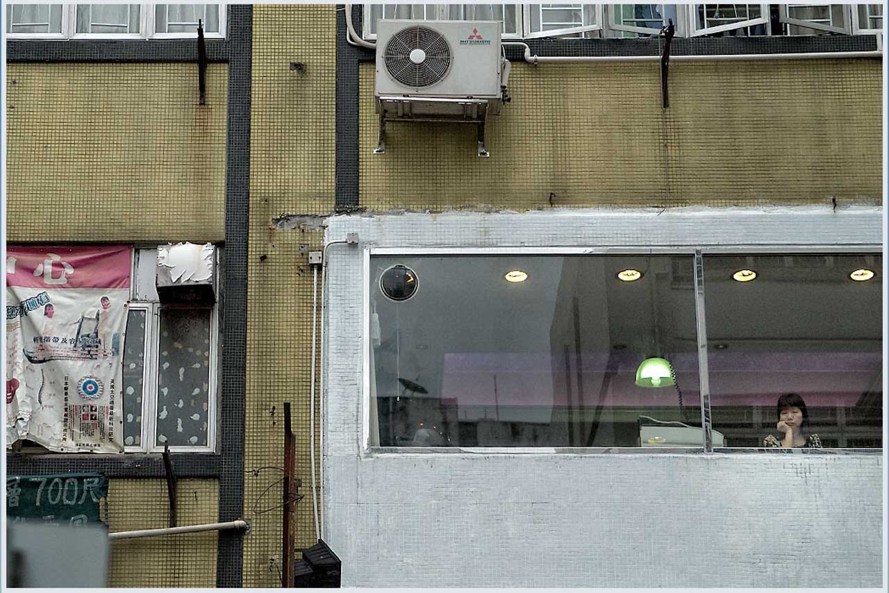 Frau schaut aus einem Fenster auf eine urbane Fassade – Symbol für innere Reflexion und Isolation.