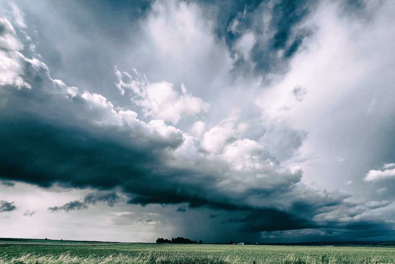 weite feldlandschaft unter wolken, die sich wie sprechfalten am horizont ausbreiten