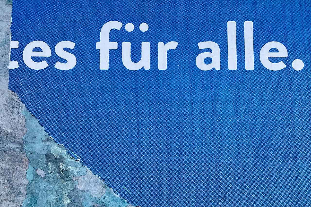 Abblätterndes Plakat mit dem Text „für alle“ auf blauem Grund