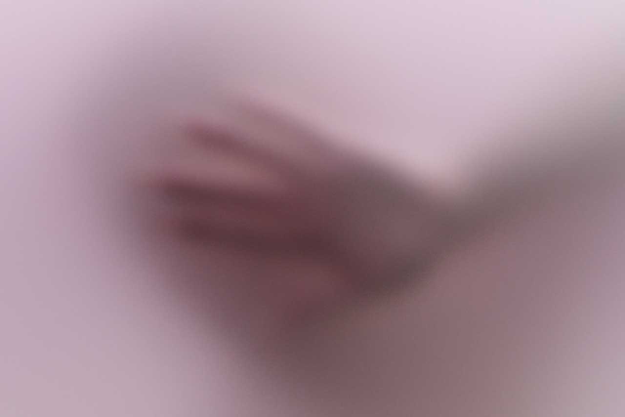 unscharfe hand hinter matter oberfläche, zarte schemen einer bewegung, stiller raum zwischen sichtbarkeit und verschwinden