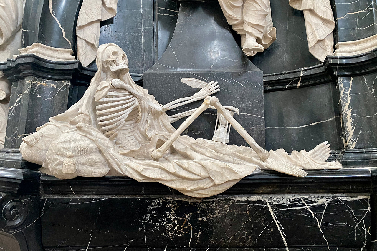 liegendes skelett in hellem stein vor dunklem marmor, ruhige pose, gefaltete stoffform, kontemplative weite