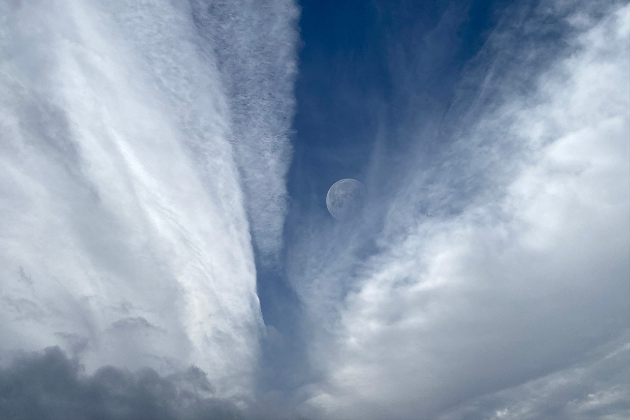 blasser halbmond im tiefblau zwischen zwei aufgerissenen wolkenfeldern, ruhig, weit, atmend